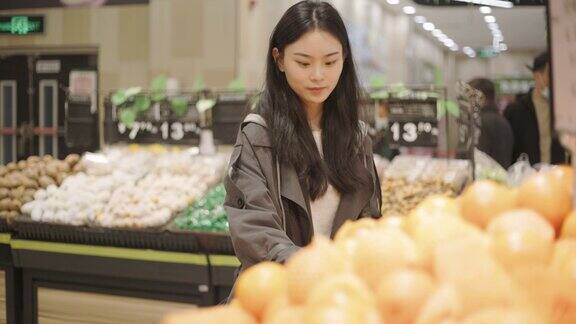 年轻的亚洲妇女在超市买水果站在橘子摊前采摘