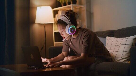 戴着耳机的年轻亚洲女子正在家里玩网络游戏