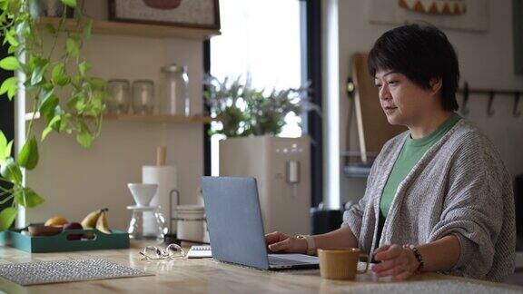 亚洲成熟的中国女性在厨房柜台用笔记本电脑工作
