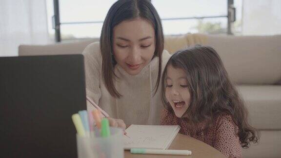 亚洲母亲帮助学龄前的女儿女孩在家里使用笔记本电脑电子学习放大在线虚拟课堂家庭教育新常态