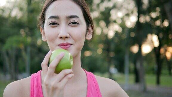 运动亚洲女人在公园吃青苹果有保健理念的女性