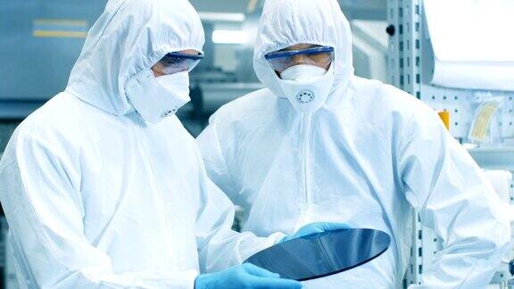 两名工程师科学家技术员穿着无菌服检查半导体硅片他们在一家现代半导体制造厂工作