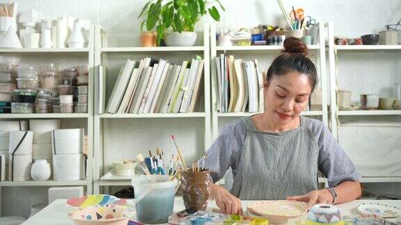 4K亚洲妇女喜欢在陶器作坊工作室画自制的陶器盘子