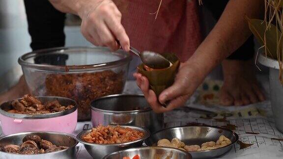 一位年长的亚洲华人妇女在她的厨房里准备粽子把配料包好为端午节做准备