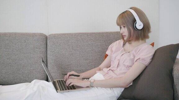 一个亚洲女人坐在沙发上用笔记本电脑在家里学习电子学习