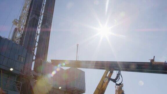 一个阳光明媚的早晨在一个石油和天然气钻井平台上一个输送升降机从井架上移除管道的倾斜镜头