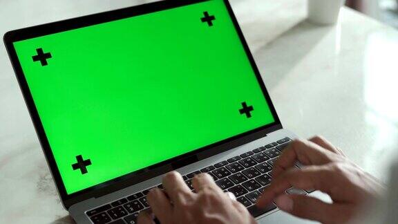 一名男子在家里的桌子上使用绿色屏幕的笔记本电脑