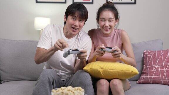 年轻的亚洲夫妇在沙发上玩电子游戏在家里玩得很开心