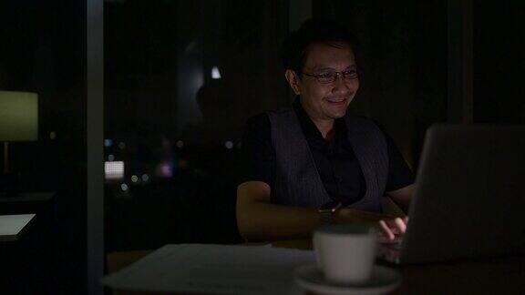 年轻的亚洲商人晚上在办公室用笔记本电脑工作的肖像