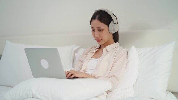 亚洲女商人在床上使用科技笔记本电脑和耳机进行在线学习