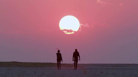 博茨瓦纳两名圣布须曼人正穿过Makgadikgadipan身后是夕阳西下的红色天空