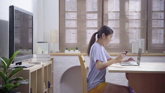 亚洲女性坐在客厅使用笔记本电脑和信用卡购买网上购物在公寓