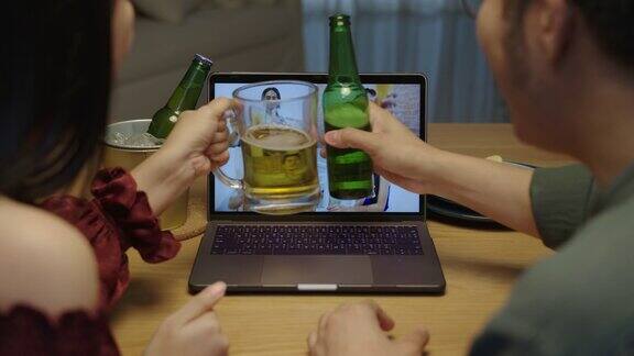 慢动作:年轻快乐的亚洲夫妇享受放松的夜晚派对活动在线庆祝节日与朋友在家里用玻璃杯和瓶子碰杯敬酒通过视频电话喝