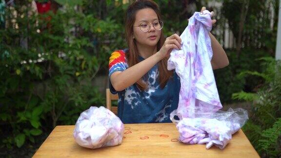年轻的亚洲妇女练习在白色t恤上处理扎染织物在家里家庭教育成功的手势
