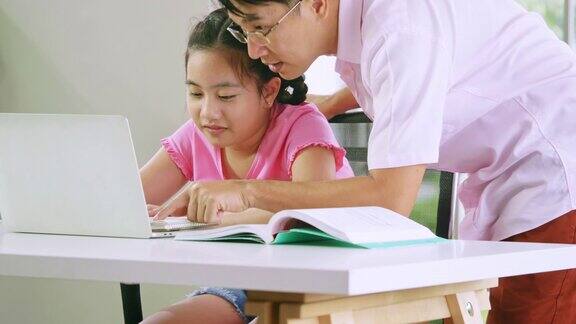 父亲在教他的女儿做家庭作业在网上远程学习在家