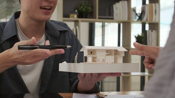建筑师指着房子模型向办公室的同事解释建筑工程的细节