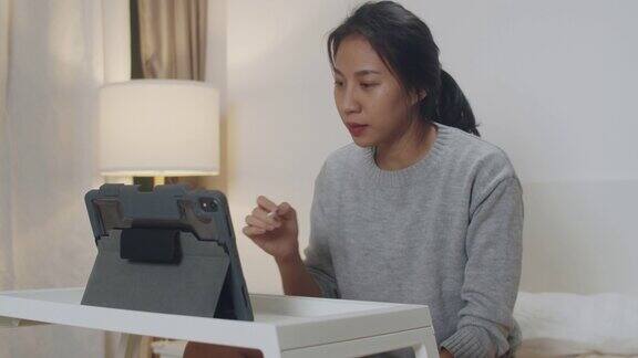 亚洲女商人使用平板电脑与同事进行视频通话同时在卧室的床上智能工作