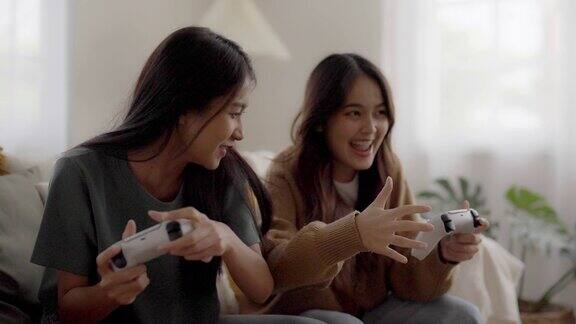 两个人年轻漂亮的亚洲女人坐在沙发上拿着摇杆遥控器在客厅玩在线视频游戏