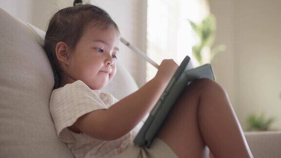 小女孩坐在沙发上喜欢用电子笔在平板上画画