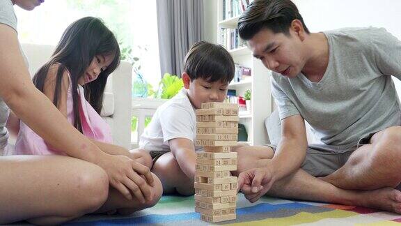 亚洲父母和两个孩子坐在地板上一起玩木制玩具