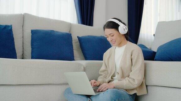 年轻的亚洲妇女戴着耳机在家里用笔记本电脑工作在家办公视频会议视频通话学生在线学习