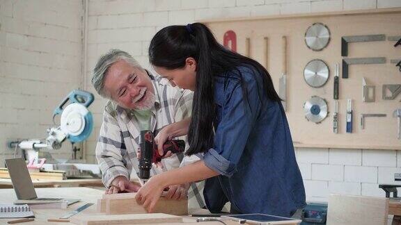 亚洲资深男青年女木匠在家庭车间建造现代家具男人和女人用电钻钻木头