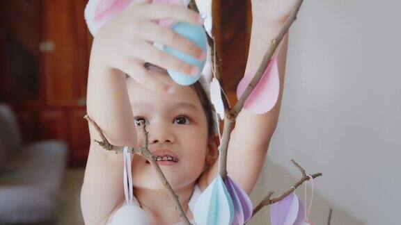 亚洲孩子女孩挂彩色的复活节彩蛋在树枝上并帮助她的父母装饰房间为复活节假期