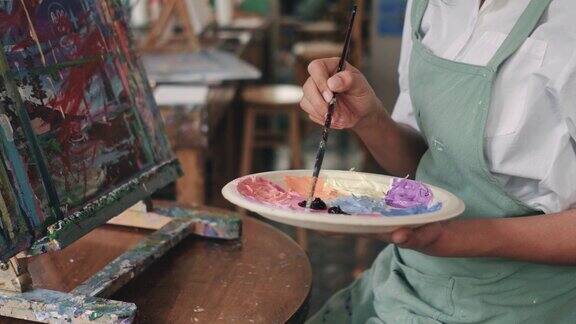 女子在画室里用油画颜料在画布上作画女艺术家在车间画画年轻的女艺术家在家里拿着调色板用画笔在画布上作画