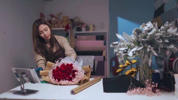 亚洲华人女花商包装红玫瑰花束在她的花店柜台为客户订购