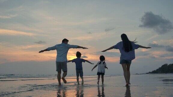 剪影快乐的亚洲家庭玩和有乐趣的海滩上日落缓慢的运动家庭、自由和旅行