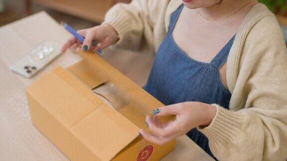 微笑的年轻亚洲女子在网上购物手里拿着智能手机收到一个送货上门的包裹网上购物