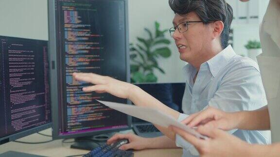 一群亚洲人软件开发人员坐在办公桌前用电脑写代码办公室里有多个屏幕程序员开发