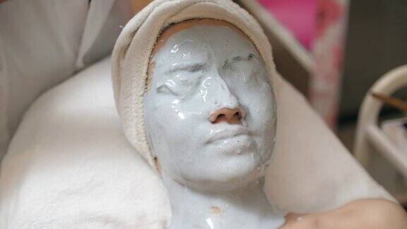 年轻的亚洲女性在水疗中心用维他命面膜按摩脸部
