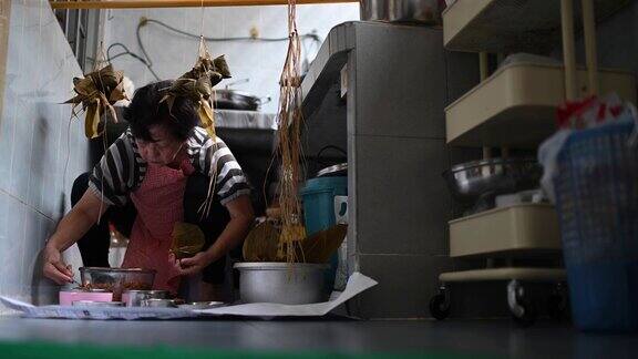 一位年长的亚洲华人妇女在她的厨房里准备粽子把配料包好为端午节做准备