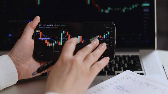 股票交易员在书桌上写在笔记本上的收盘与股票价格数据显示在智能手机上对比新旧股票经纪人正在看屏幕上的数据金融分析师的工作