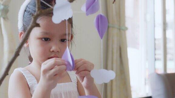 亚洲女孩帮助她的父母用花环装饰房间挂在树枝上复活节假期