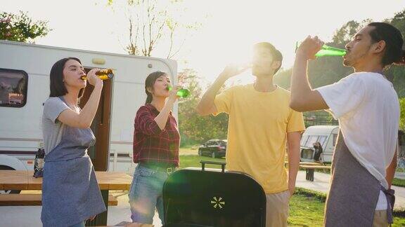 一群亚洲男女在晚上一起举行户外新年派对朋友们喝着一瓶啤酒带着幸福和微笑喝着旅行自然露营车露营