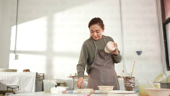 4K亚洲妇女喜欢在陶器作坊工作室画自制的陶瓷马克杯