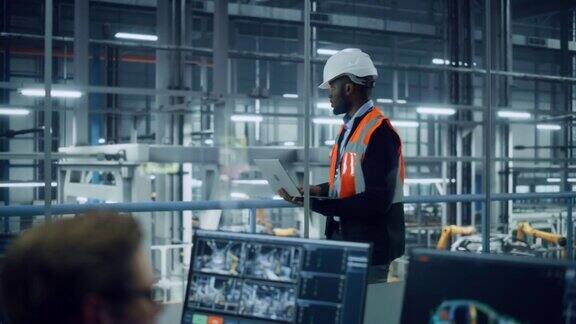 非裔美国工程师在汽车装配厂使用笔记本电脑和向外看汽车工厂生产线操作员在办公桌上工作俯瞰自动电动汽车的生产
