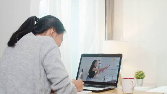 年轻的亚洲少女大学学生使用笔记本电脑远程学习与女教师远程教学在互联网上在家里