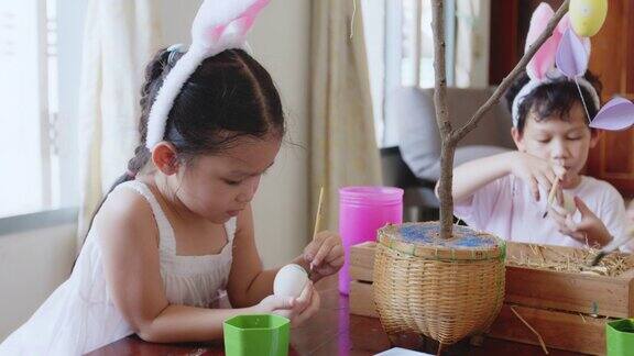 亚洲女孩打扮成兔子头带和她的家人在鸡蛋上着色孩子和家人准备复活节画和装饰蛋