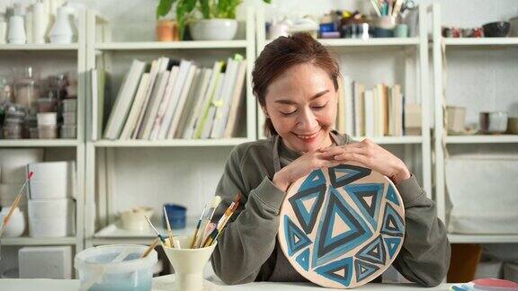 4K肖像的亚洲妇女绘画她自制的陶瓷板在陶艺工作室