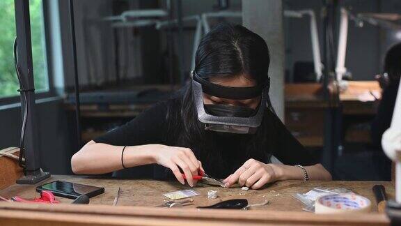 亚洲韩国女学生在大学工作台上用放大镜缝制珠宝