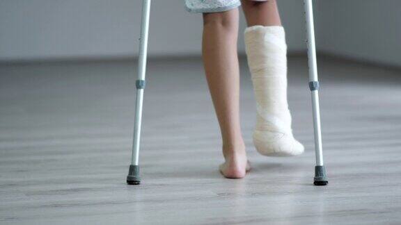 年轻女子拄着拐杖摔断了一条腿打了石膏在家里走路断腿事故后康复