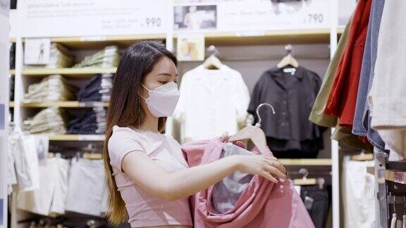 戴着防护口罩的亚洲妇女在服装店挑选衣服