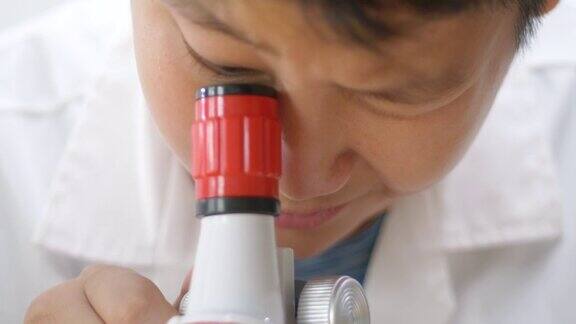 亚洲男孩穿着实验服在学校实验室使用显微镜进行测试教育的生活方式理念