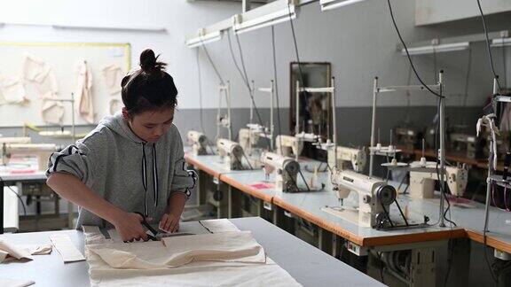 亚洲华裔时装女大学生在大学工作坊裁剪面料做服装项目