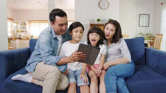快乐快乐的亚洲家庭爸爸妈妈和孩子在家里的沙发上玩数码平板视频通话