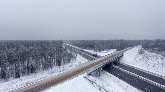 一辆红色轿车和几辆卡车正行驶在白雪覆盖的森林中央的高速公路上