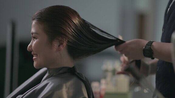 美发沙龙亚洲华人女性发型师在美发沙龙为她的顾客剪发梳理湿长发